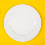 Aerial view of a white place on a yellow table next to silverware
