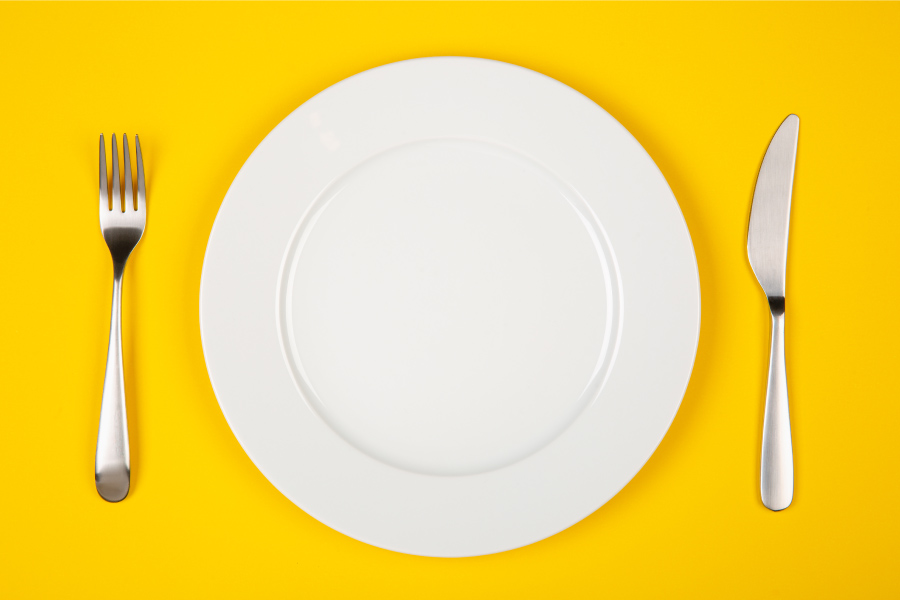 Aerial view of a white place on a yellow table next to silverware